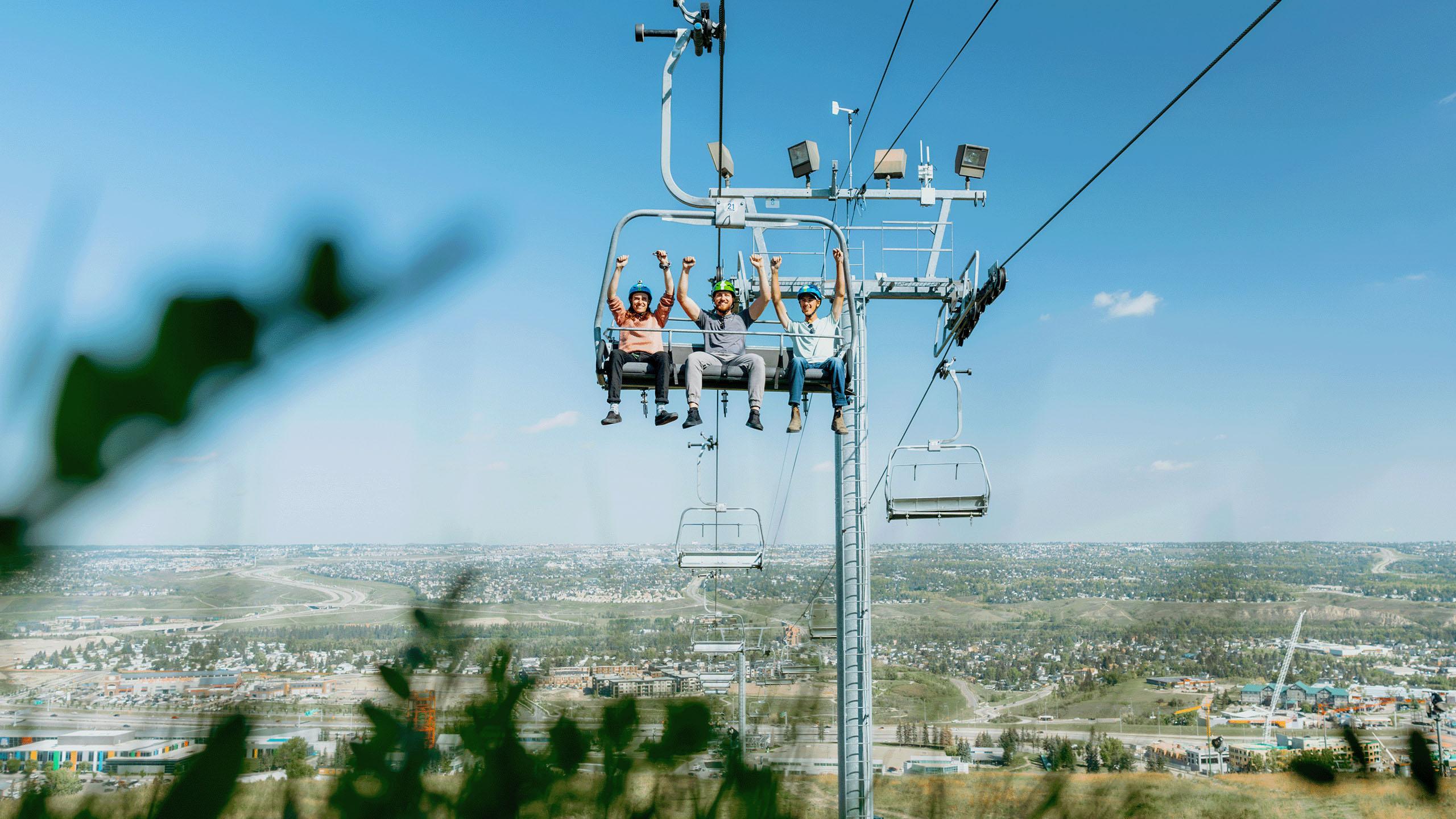 Three friends raise their arms in the air whilst riding the chairlift at Downhill Karting Calgary.